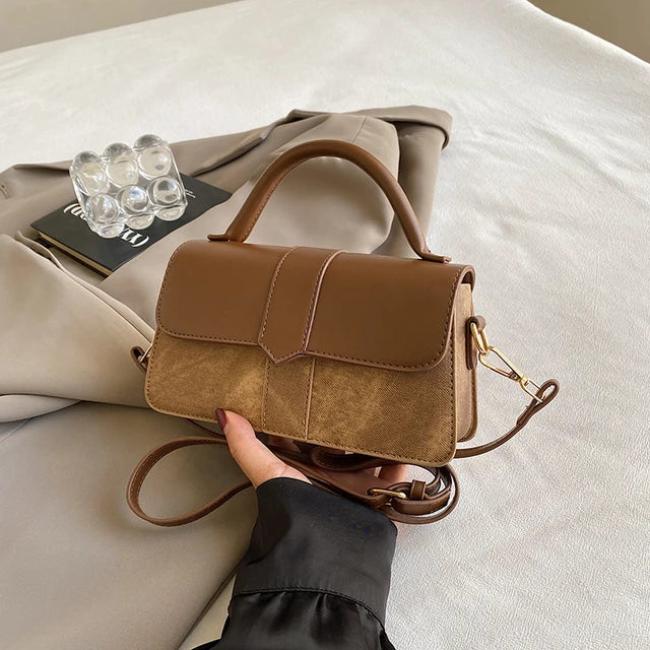 Borsa a tracolla in pelle marrone su giacca beige, design elegante, manico superiore, chiusura a patta, accessorio moda donna, stile casual chic.