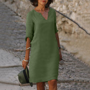 Donna con abito verde oliva a maniche lunghe, scollo a V, su strada acciottolata. Accessori: cappello, bracciali. Moda casual elegante.