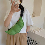 Donna con borsa a tracolla verde a forma di baccello di pisello, indossa maglietta bianca e pantaloni beige. Accessorio moda originale e trendy.