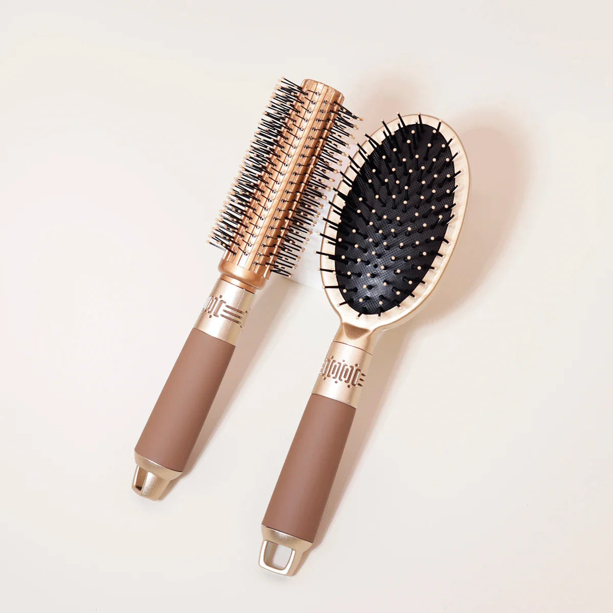 Due spazzole per capelli dorate su sfondo chiaro, una rotonda e una ovale, ideali per styling e cura dei capelli. Accessori bellezza professionali.