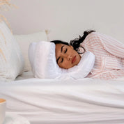 Donna che dorme su un cuscino ergonomico bianco a forma di C, indossando pigiama a righe rosa, in una camera da letto minimalista.