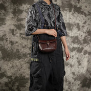 Persona con tuta nera e camicia a motivi geometrici, indossa una borsa a tracolla in pelle marrone. Stile casual, moda urbana, accessori vintage.