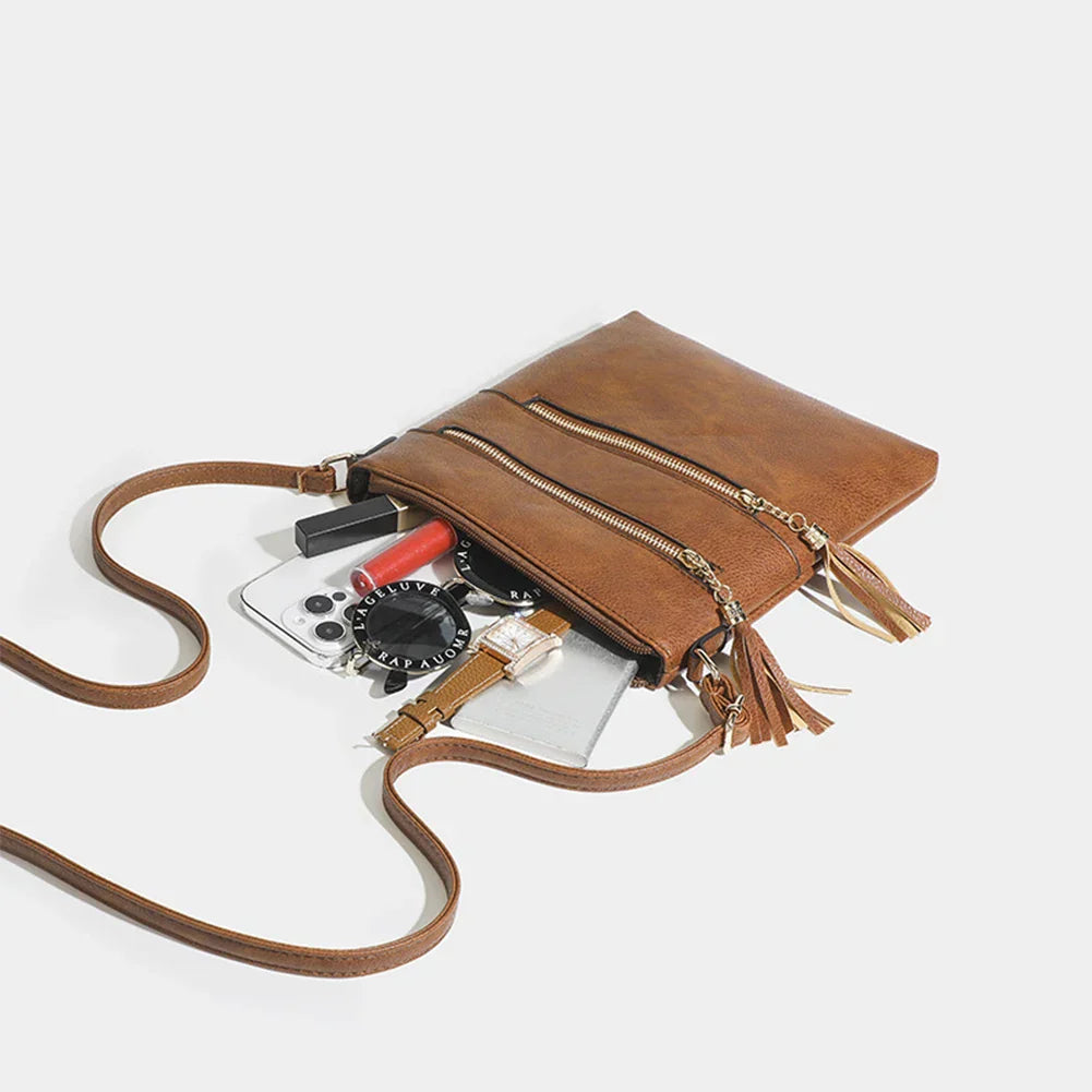 Borsa a tracolla in pelle marrone con cerniere dorate, contenente smartphone, rossetto e portafoglio. Accessorio moda donna elegante e pratico.