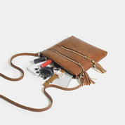 Borsa a tracolla in pelle marrone con cerniere dorate, contenente smartphone, rossetto e portafoglio. Accessorio moda donna elegante e pratico.