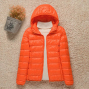 Giacca invernale arancione con cappuccio, imbottita, su sfondo beige. Moda donna, abbigliamento caldo, stile casual.