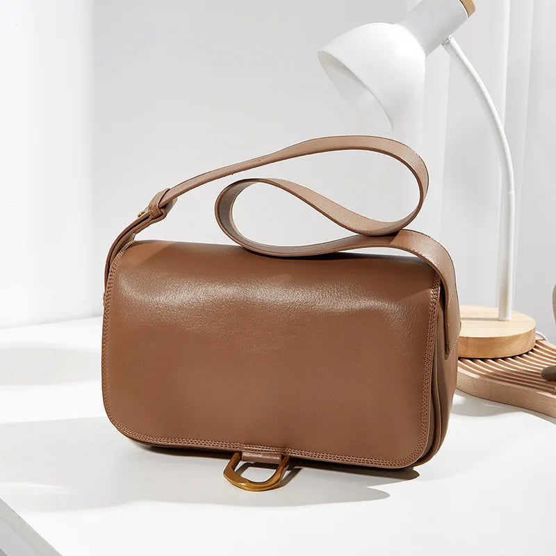Borsa a tracolla in pelle marrone su tavolo bianco, design elegante, chiusura con fibbia dorata, ideale per moda donna, accessorio di tendenza.