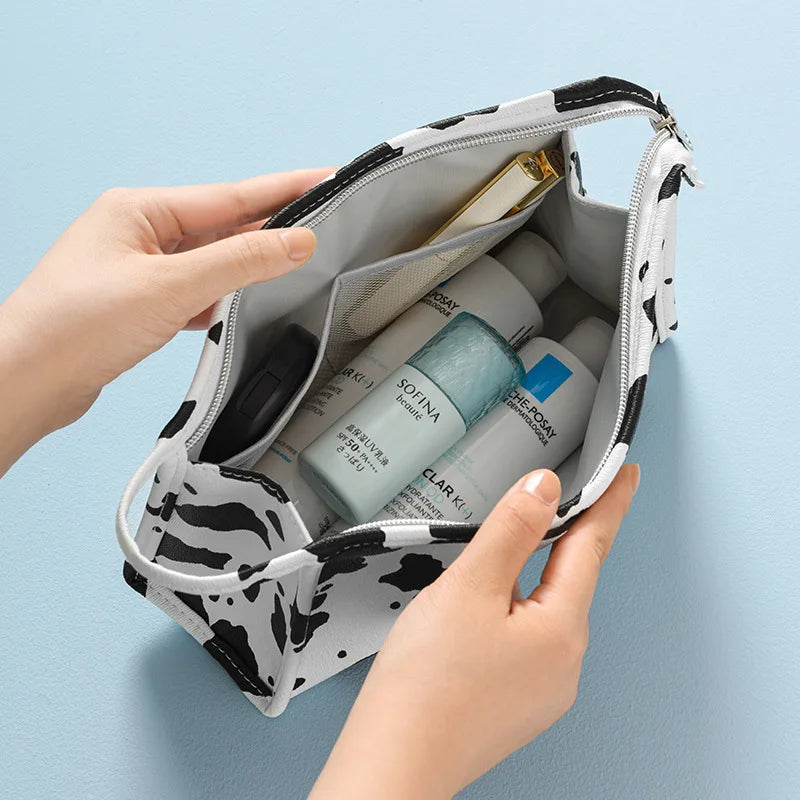 Borsa cosmetica bianca e nera con cerniera, contenente flaconi di prodotti per la cura della pelle, su sfondo azzurro. Accessori bellezza viaggio.