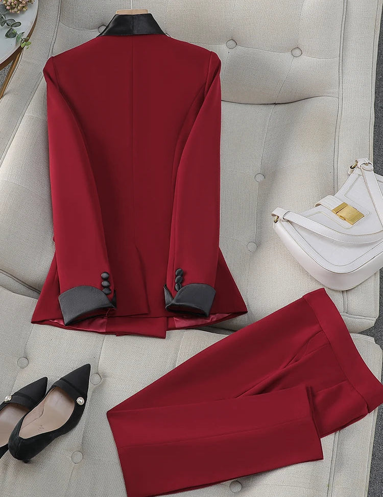 Completo elegante rosso da donna su divano beige, con giacca e pantaloni abbinati. Accessori: borsa bianca e scarpe nere con tacco.