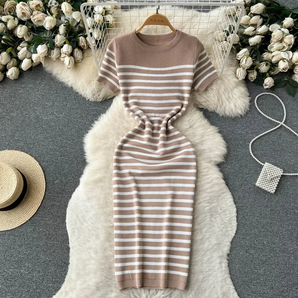 Abito a righe beige e bianche su tappeto peloso bianco, circondato da rose bianche e accessori moda. Elegante e casual, perfetto per ogni occasione.