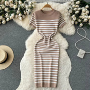 Abito a righe beige e bianche su tappeto peloso bianco, circondato da rose bianche e accessori moda. Elegante e casual, perfetto per ogni occasione.