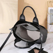 Borsa a mano nera in pelle con interno beige, cerniera aperta, manici robusti e tracolla regolabile, su sfondo chiaro. Accessorio moda elegante.