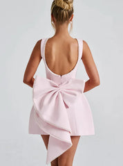 Abito rosa elegante con fiocco posteriore, scollatura profonda, dettagli perle, moda donna, abbigliamento da sera, stile sofisticato.