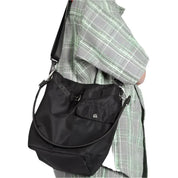 Borsa a tracolla nera in nylon, indossata su camicia a quadri verde e grigia. Design moderno, tasca frontale con bottone, ideale per uso quotidiano.