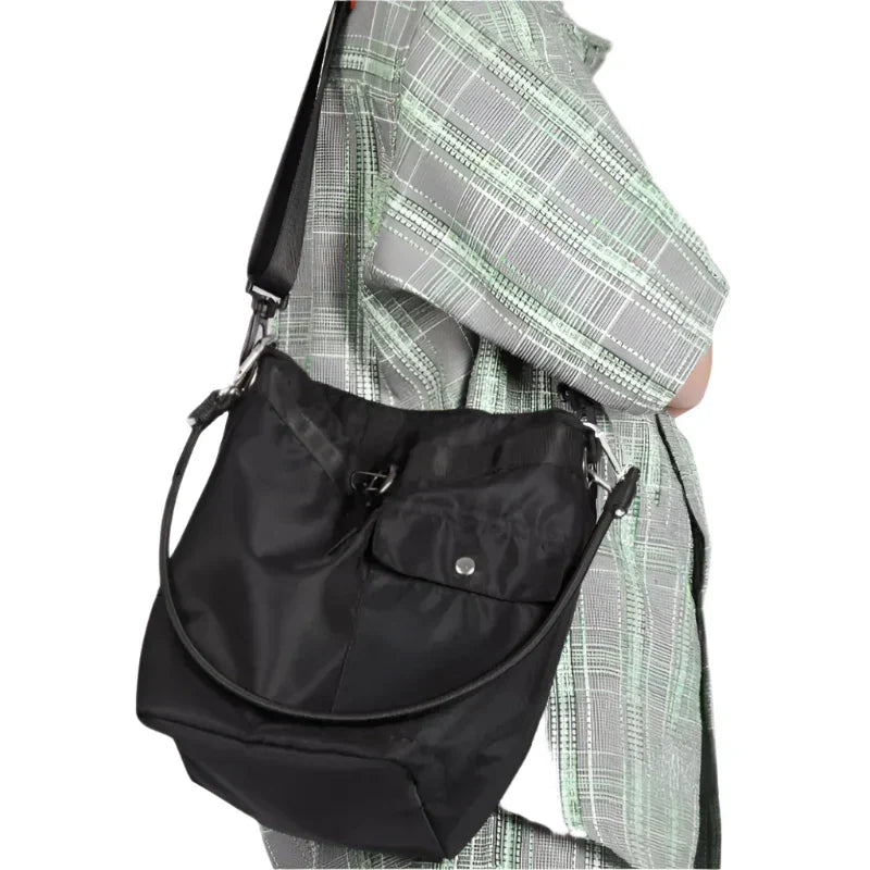 Borsa a tracolla nera in nylon, indossata su camicia a quadri verde e grigia. Design moderno, tasca frontale con bottone, ideale per uso quotidiano.