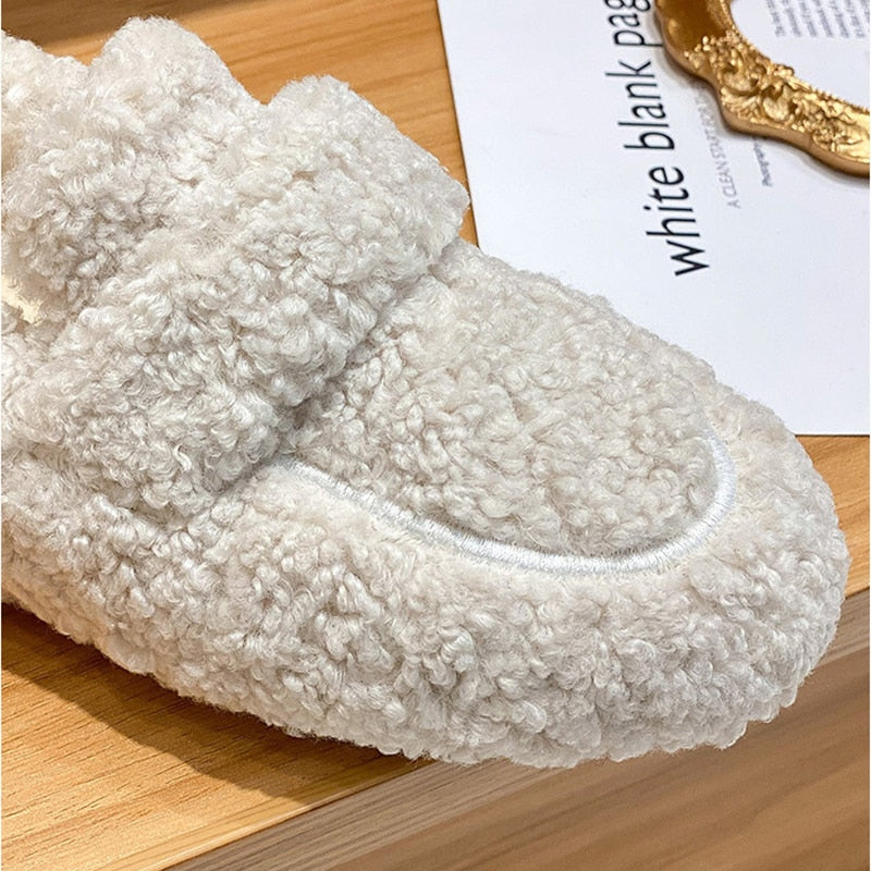 Pantofole in pelliccia sintetica beige su tavolo di legno, design morbido e caldo, ideali per l'inverno. Accessorio moda casa confortevole.