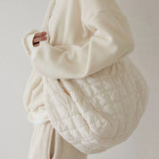 Borsa trapuntata beige oversize in tessuto morbido, indossata da una persona in abbigliamento coordinato. Accessorio moda casual e versatile.