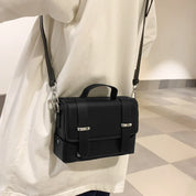 Borsa a tracolla nera in pelle, design elegante e compatto, indossata su camicia bianca. Accessorio moda unisex, ideale per ogni occasione.