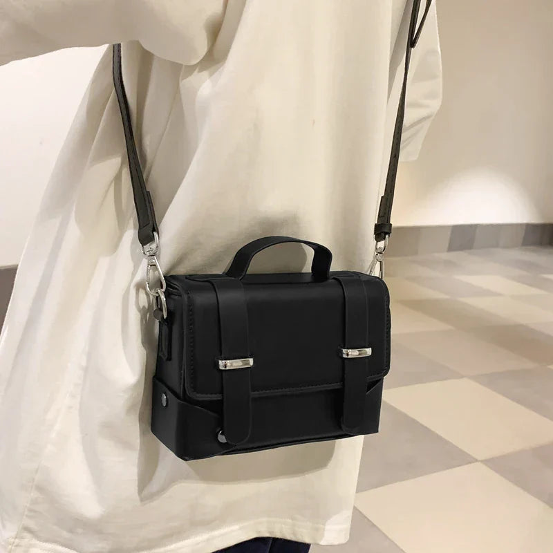 Borsa a tracolla nera in pelle, design elegante e compatto, indossata su camicia bianca. Accessorio moda unisex, ideale per ogni occasione.