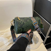 Borsa a tracolla cilindrica verde con motivo floreale in rilievo, cinturino regolabile decorato, chiusura con zip dorata. Accessorio moda elegante.