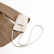 Borsa a tracolla beige minimalista su giacca marrone, design elegante in pelle, accessorio moda donna, stile contemporaneo.