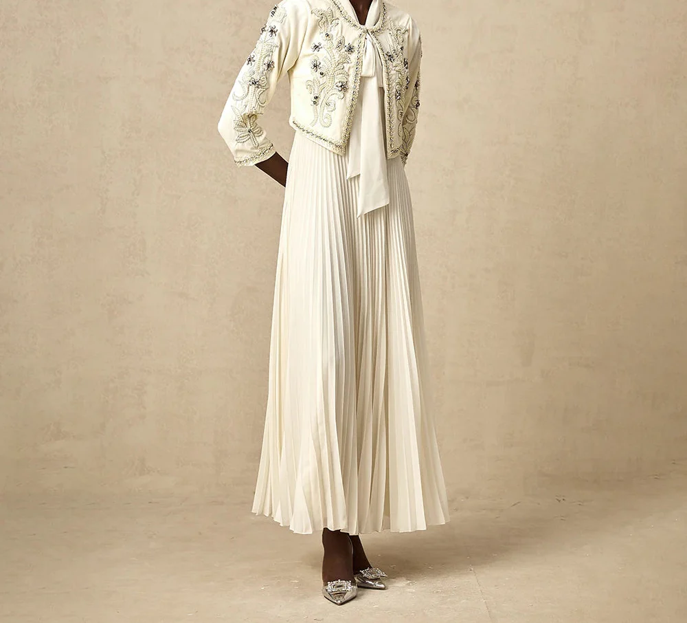 Abito lungo bianco elegante con giacca ricamata, maniche a tre quarti, gonna plissettata, scarpe con tacco. Moda femminile sofisticata.