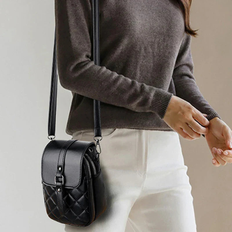 Donna con borsa a tracolla nera in pelle trapuntata, indossa maglione grigio e pantaloni bianchi. Accessorio moda elegante e versatile.
