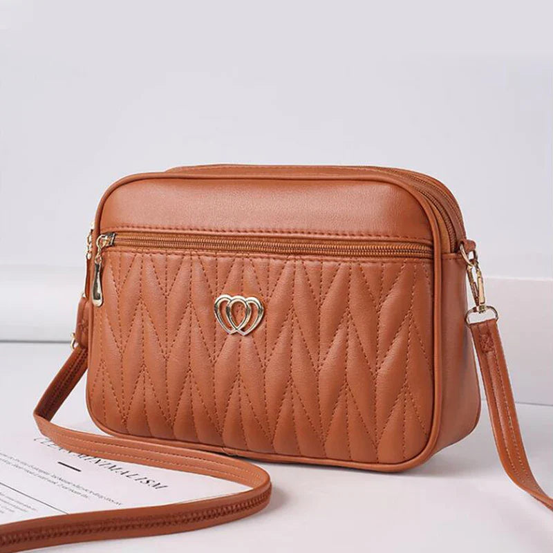Borsa a tracolla in pelle marrone con motivo trapuntato e cerniera frontale, decorata con un piccolo logo a forma di cuore. Elegante e versatile.