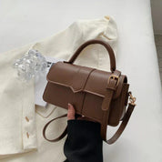 Borsa a tracolla in pelle marrone su giacca bianca, con manico e fibbia dorata. Accessorio moda elegante per donna.