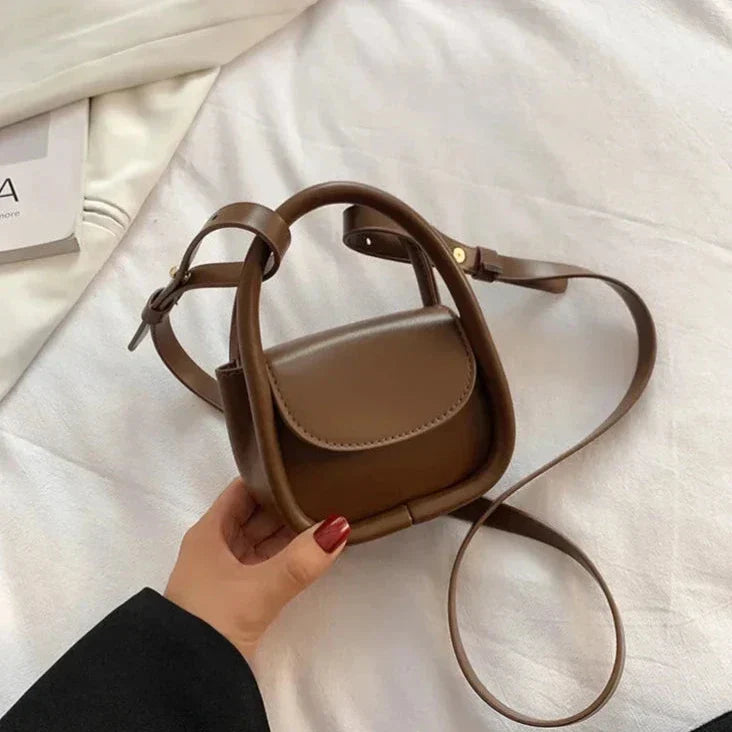 Borsa a tracolla marrone in pelle, design minimalista, su letto bianco. Accessorio moda donna elegante, perfetto per ogni occasione.