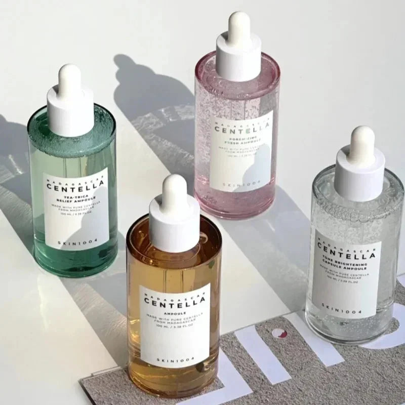 Bottiglie di siero Centella SKIN1004 in vetro con contagocce, varianti colorate. Prodotti skincare coreani per idratazione e cura della pelle.