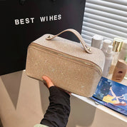 Borsa cosmetica beige glitterata con manico, chiusura a zip, su sfondo di prodotti di bellezza. Elegante e pratica per organizzare trucchi e accessori.