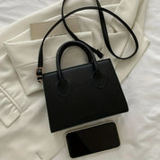 Borsa a mano nera elegante su giacca bianca, con smartphone e libro. Accessorio moda donna, stile minimalista, pelle sintetica.