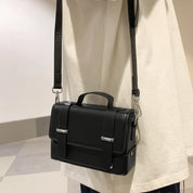 Borsa a tracolla nera in pelle, design elegante e moderno, con fibbie argentate, indossata su maglietta bianca. Accessorio moda unisex.
