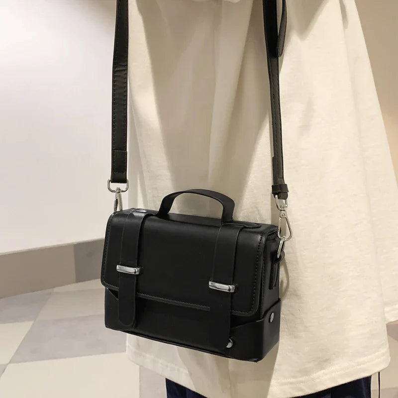 Borsa a tracolla nera in pelle, design elegante e moderno, con fibbie argentate, indossata su maglietta bianca. Accessorio moda unisex.