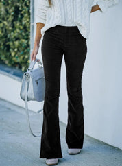 Donna con maglione bianco e pantaloni a zampa neri, borsa grigia, sfondo urbano. Moda autunnale, abbigliamento casual elegante.