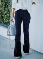 Donna con maglione bianco e pantaloni a zampa blu scuro, borsa grigia a tracolla, sfondo urbano. Moda autunnale, abbigliamento casual elegante.