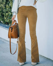 Pantaloni a zampa marroni in velluto a coste, abbinati a maglione bianco e borsa in pelle marrone. Moda autunnale casual donna.
