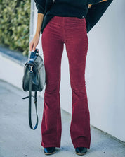 Donna con pantaloni a zampa bordeaux, maglione nero, borsa a tracolla nera e stivali neri. Moda autunnale, abbigliamento casual elegante.