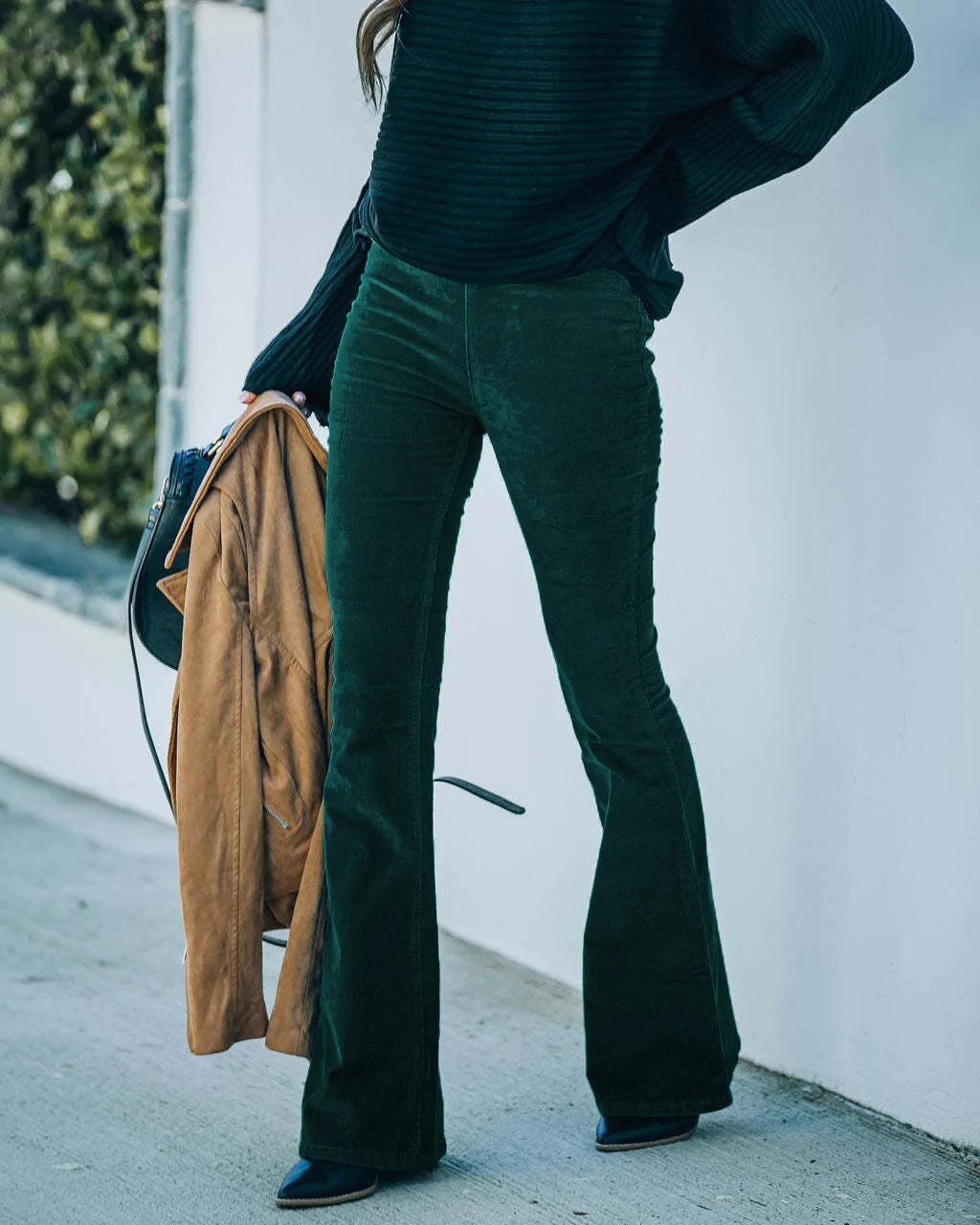 Pantaloni a zampa verde scuro in velluto a coste, donna, moda autunno, abbinati a maglione nero e giacca marrone, stile casual chic.