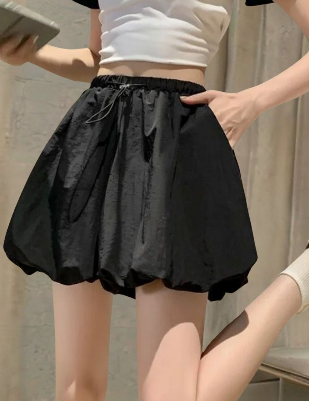 Gonna nera a palloncino, vita alta, con tasche, indossata da una donna. Moda estiva casual, tessuto leggero, abbinata a top bianco e calzini.