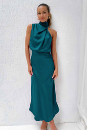 Abito lungo elegante verde smeraldo con collo alto drappeggiato, indossato da una donna sorridente su sfondo bianco. Moda femminile sofisticata.