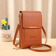 Borsa a tracolla in pelle marrone con chiusura a zip, design elegante e compatto. Perfetta per smartphone e accessori. Sfondo con pianta decorativa.