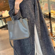 Borsa a tracolla grigia in pelle, indossata da una persona con cappotto grigio. Accessorio moda elegante, perfetto per l'autunno e l'inverno.