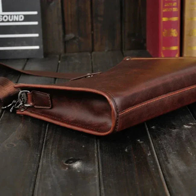 Borsa a tracolla in pelle marrone su tavolo di legno scuro, design elegante e vintage, ideale per uomo, accessorio moda, qualità artigianale.