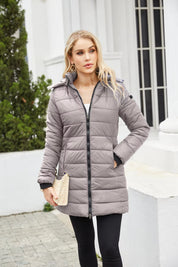 Donna con cappotto imbottito grigio, zip frontale, cappuccio, tasche laterali, posa all'aperto. Moda invernale, abbigliamento caldo, stile casual.