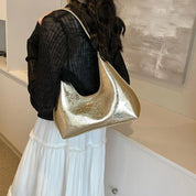 Donna con borsa a spalla dorata in pelle, indossa maglia nera e gonna bianca. Accessorio moda elegante, perfetto per look casual e chic.