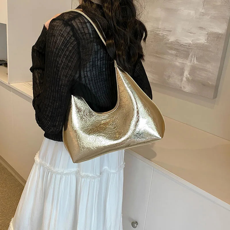 Donna con borsa a spalla dorata in pelle, indossa maglia nera e gonna bianca. Accessorio moda elegante, perfetto per look casual e chic.