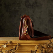 Borsa a tracolla in pelle marrone su tavolo di legno, design elegante con fibbie dorate, accessorio moda autunno, sfondo scuro.