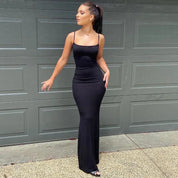 Abito lungo nero elegante, aderente, con spalline sottili, indossato da una donna davanti a un garage. Moda femminile, abbigliamento da sera.