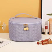 Astuccio cosmetico viola con motivo intrecciato, cerniera dorata e manico. Ideale per organizzare trucchi e accessori di bellezza.